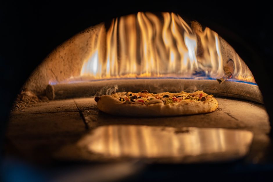 Gas pizza oven cooking a Neapolitan pizza with a visible flame