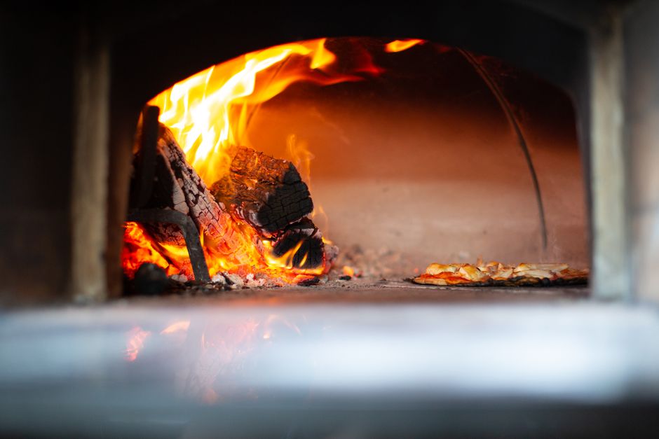 Multi-fuel pizza oven with wood flame cooking a pizza