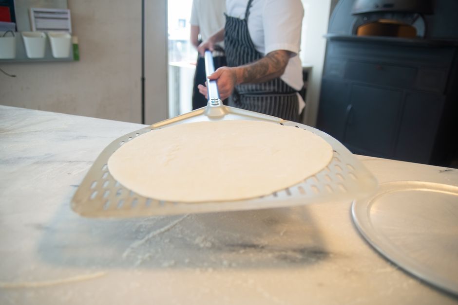 Perforated metal pizza peel with fresh dough being prepared